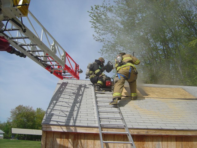 Firefighter Jeff Slotoroff instructs Junior Corp member Tim Collins on roof ventilation at the YHFD Roof Simulator  